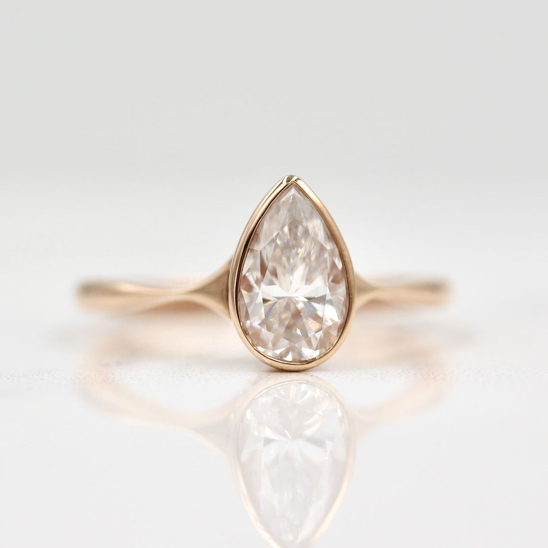 Pear shaped Diamond with a Rose Gold Band on White Background and Surface