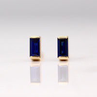 The September Baguette Birthstone Earrings with Blue Sapphire in Yellow Gold against a white background