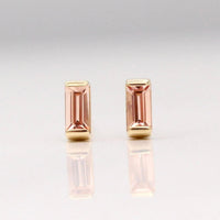 The October Baguette Birthstone Earrings with Peachy-Pink Sapphire in Yellow Gold against a white background