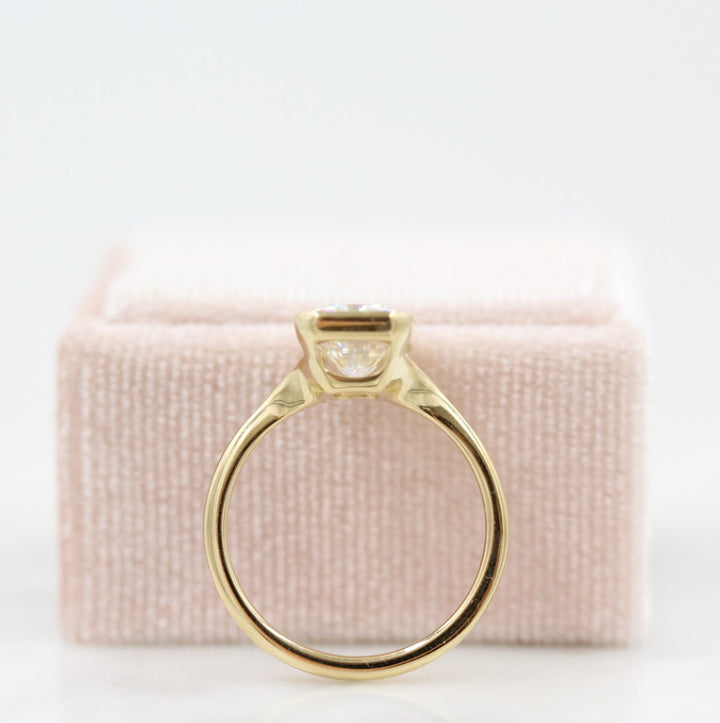 A yellow gold bezel ring resting against a light pink velvet ring box