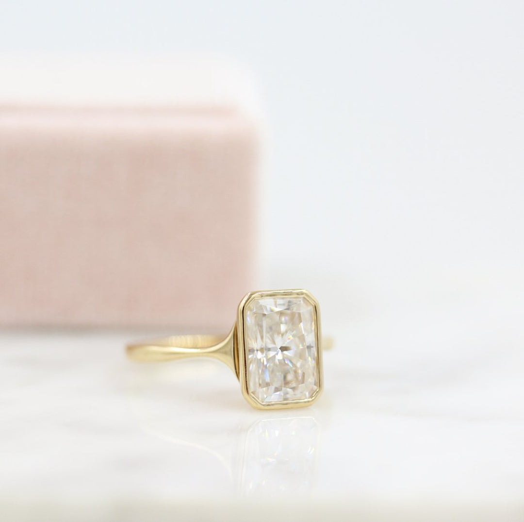 A gold radiant moissanite bezel engagement ring