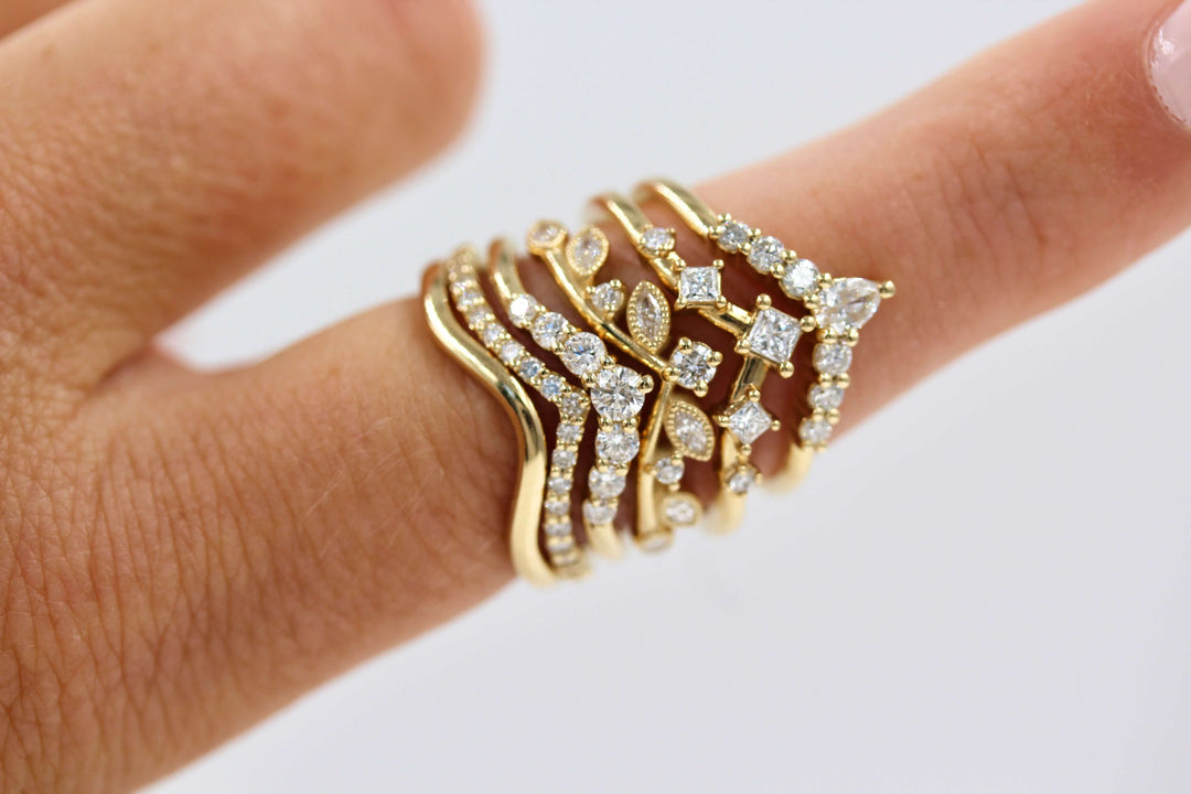 Stack of yellow gold and diamond contour wedding bands on a finger