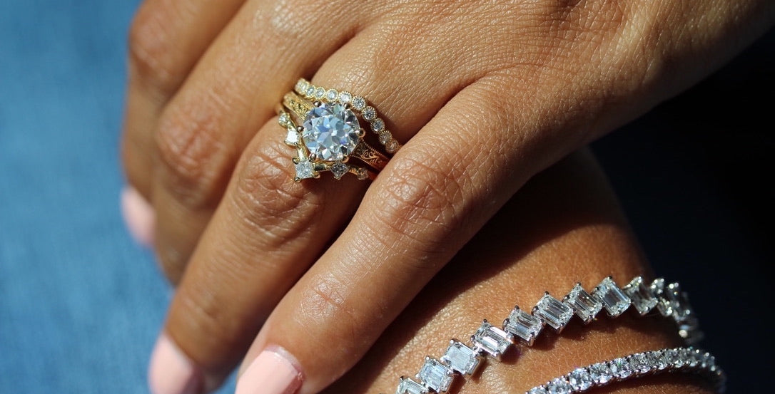 The Astra and Florence Contour Wedding Bands in yellow gold stacked with the Kathleen Ring on a hand also wearing two tennis bracelets