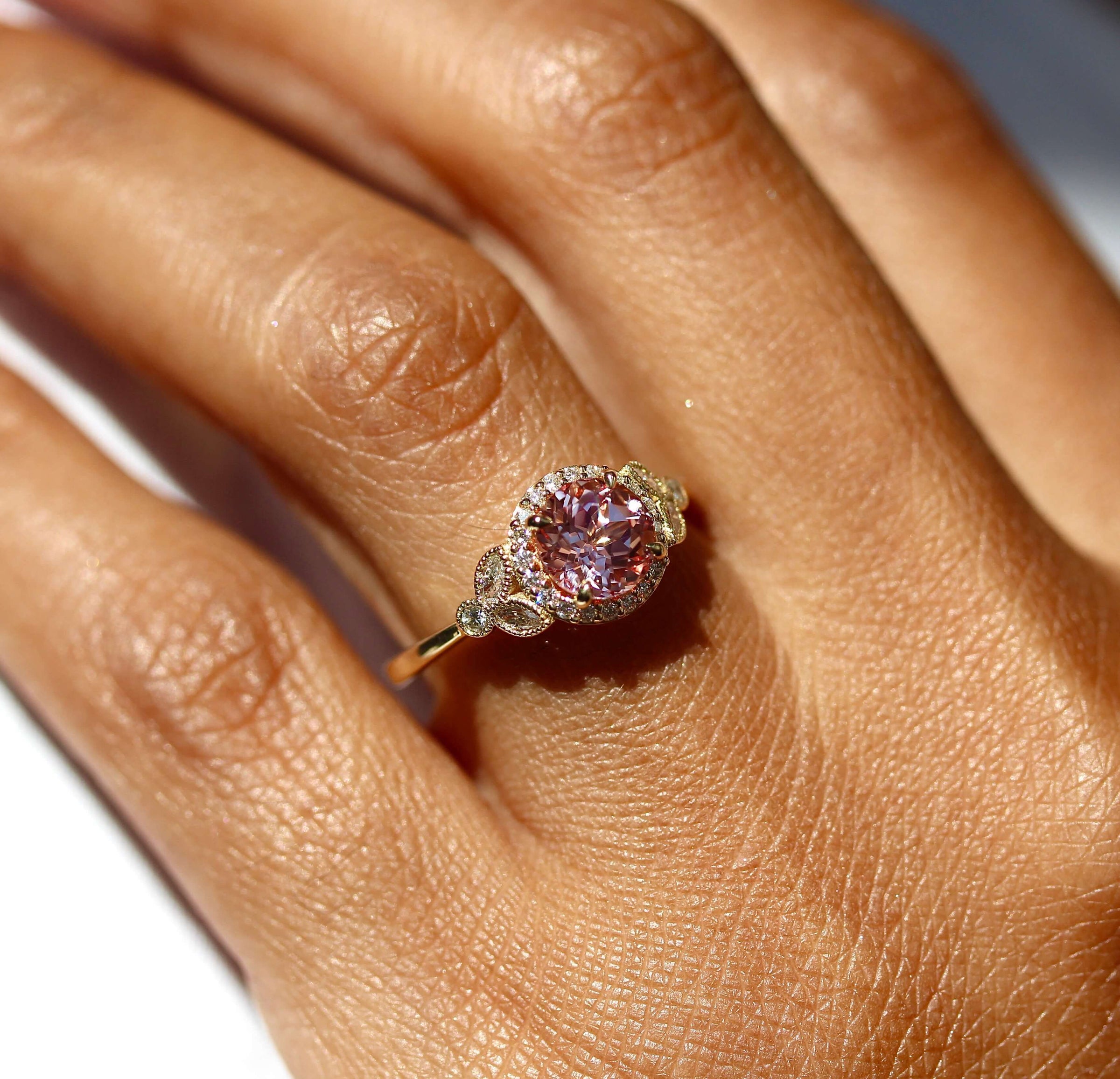 The Charlotte Ring (Round) in yellow gold and a peachy-pink created sapphire modeled on a hand