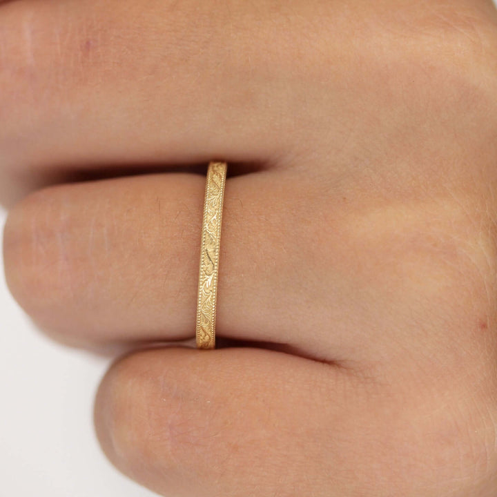14k yellow gold engraved wedding band modeled on a hand