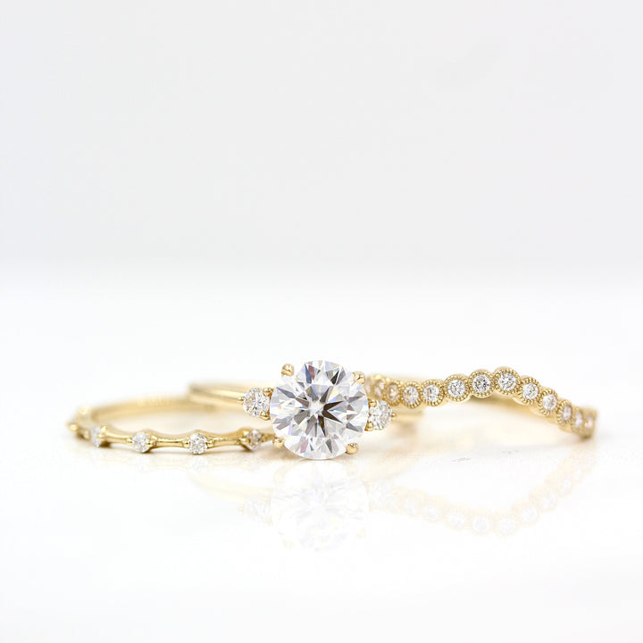 The Esme Ring (Round) in Yellow Gold with 2ct Moissanite staggered with the Florence Contour Band in yellow gold and the Sloane Wedding Band in yellow gold against a white background