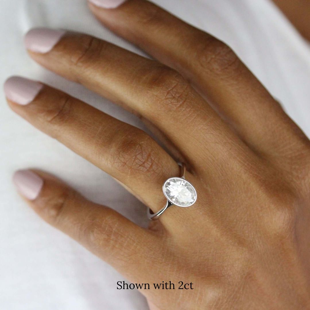 2ct oval solitaire engagement ring with delicate bezel in white gold, worn on ring finger