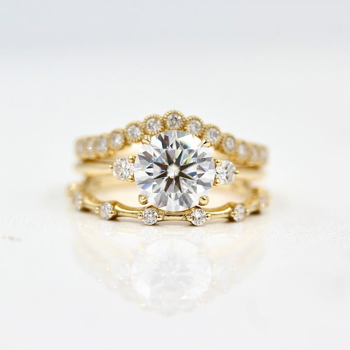 The Esme Ring (Round) in Yellow Gold with 2ct Moissanite stacked with the Florence Contour Band in yellow gold and the Sloane Wedding Band in yellow gold against a white background