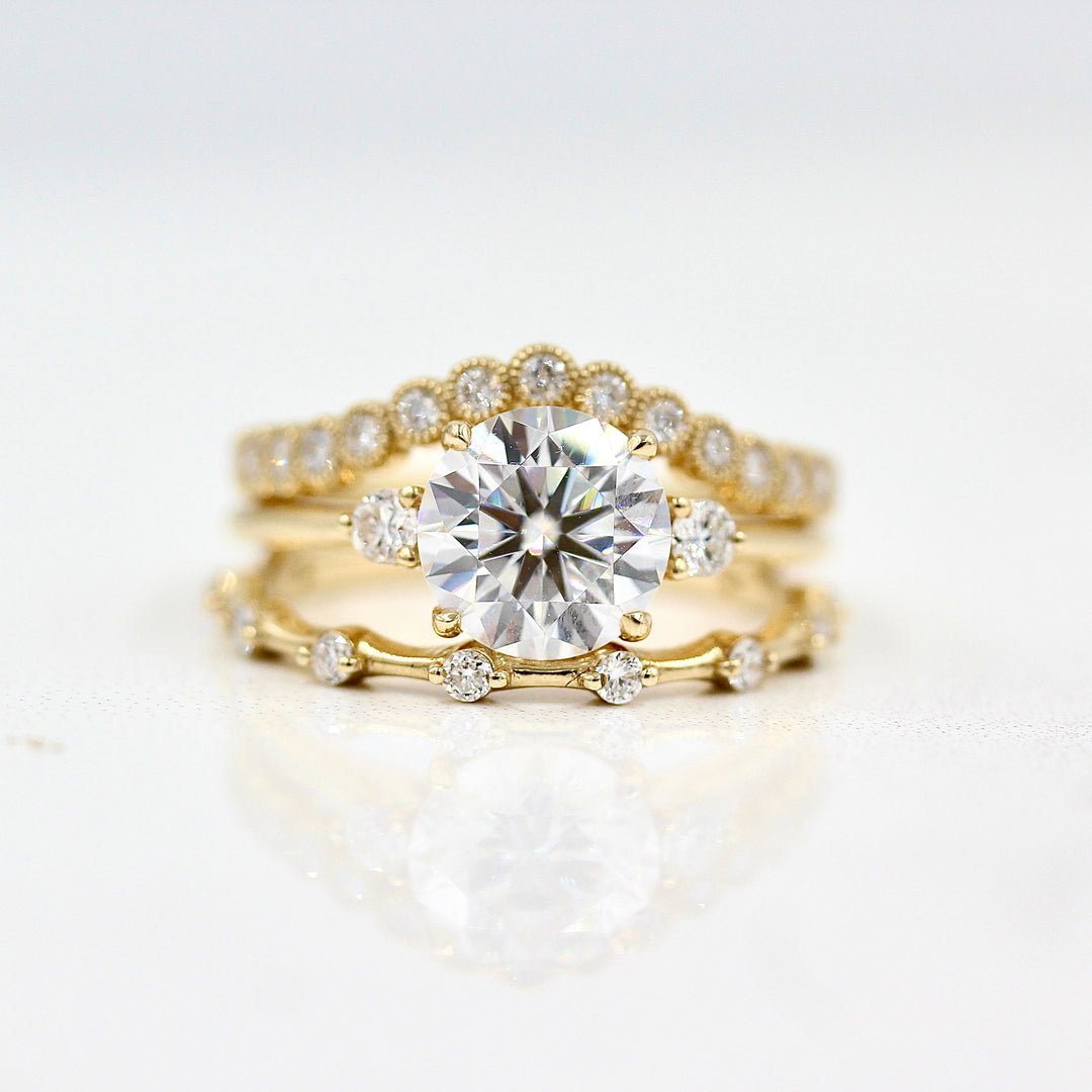 The Esme Ring (Round) in Yellow Gold with 2ct Moissanite stacked with the Florence Contour Band in yellow gold and the Sloane Wedding Band in yellow gold against a white background