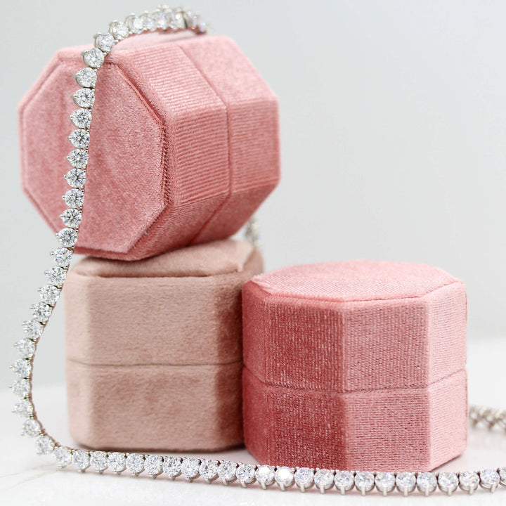 The Lab Grown Diamond Tennis Necklace in white gold draped over three pink velvet ring boxes