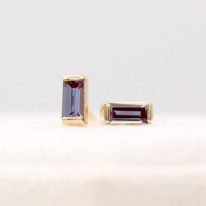 The June Baguette Birthstone Earrings with Alexandrite in Yellow Gold atop of a white velvet ring box