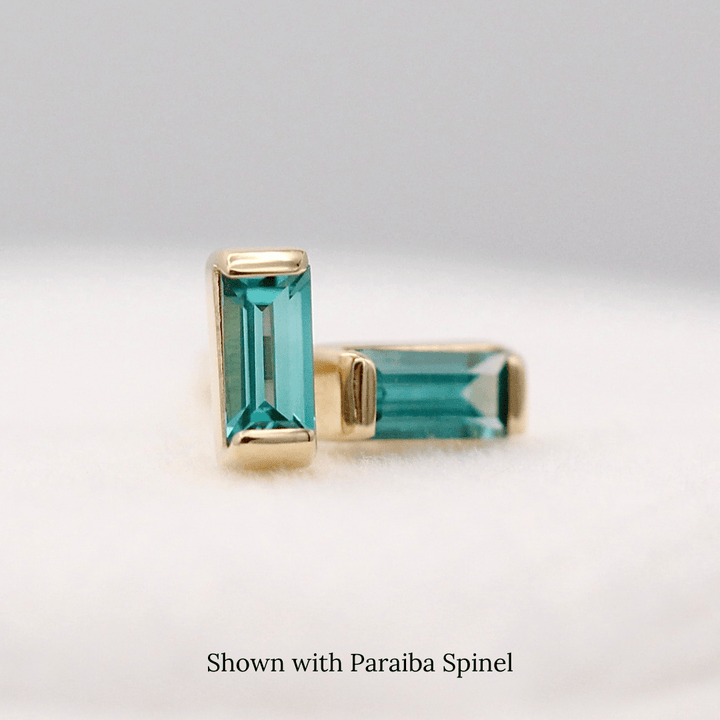 The December Baguette Birthstone Earrings with Paraiba Spinel in Yellow Gold atop of a white velvet ring box
