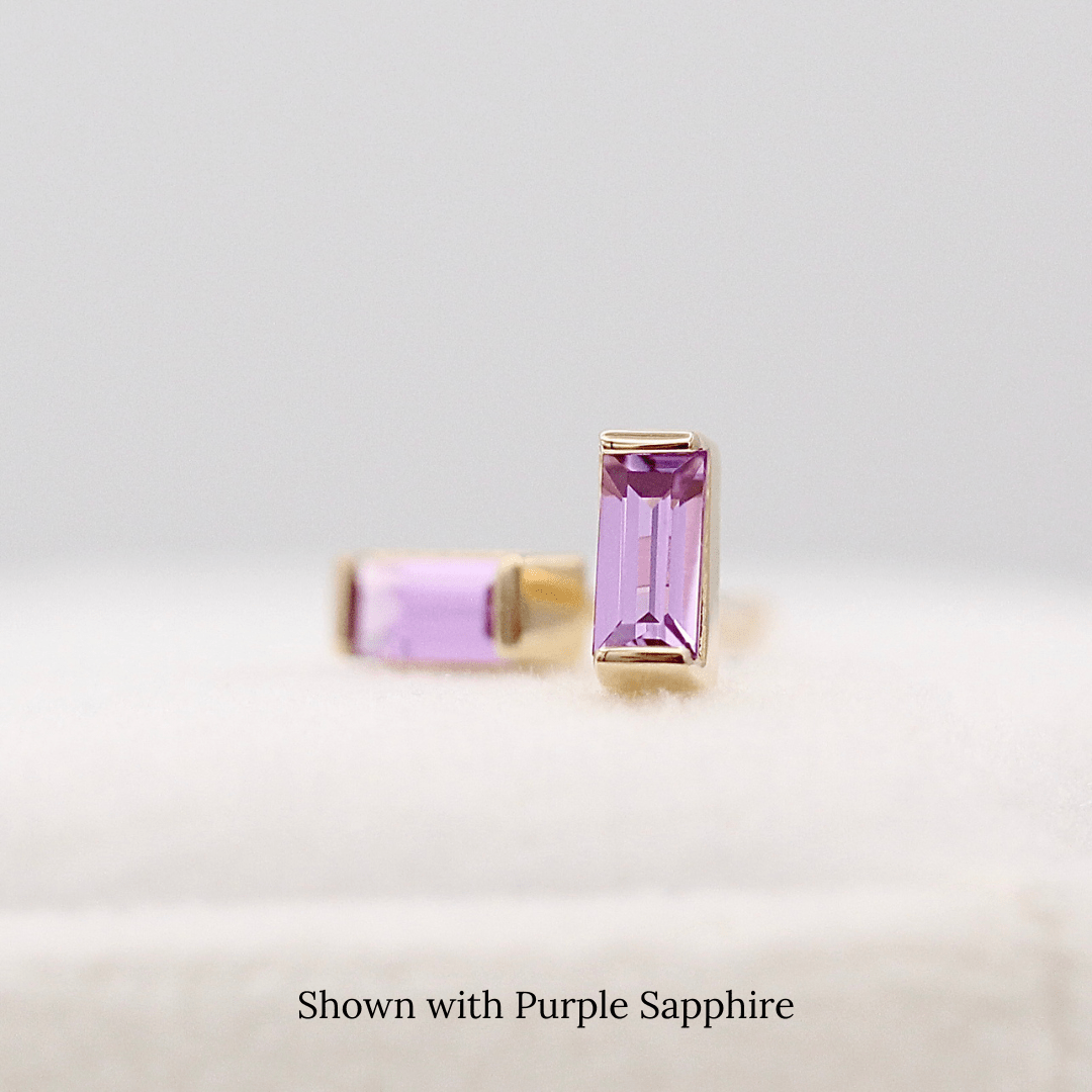 The February Baguette Birthstone Earrings with Purple Sapphire in Yellow Gold atop of a white velvet ring box