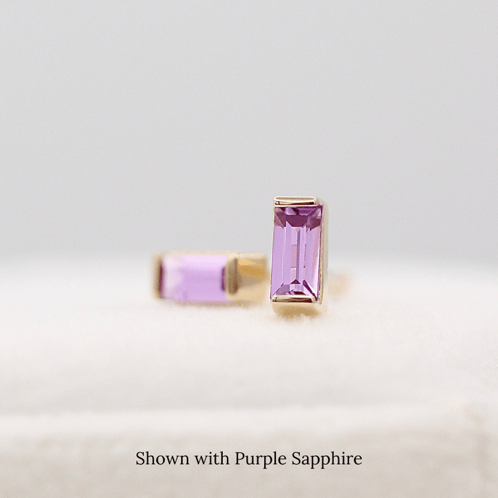 The February Baguette Birthstone Earrings with Purple Sapphire in Yellow Gold atop of a white velvet ring box
