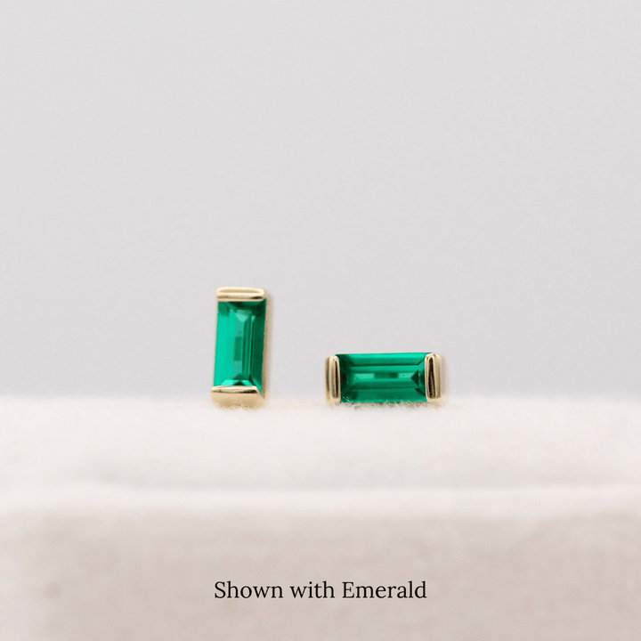 The May Baguette Birthstone Earrings with Emerald in Yellow Gold atop of a white velvet ring box
