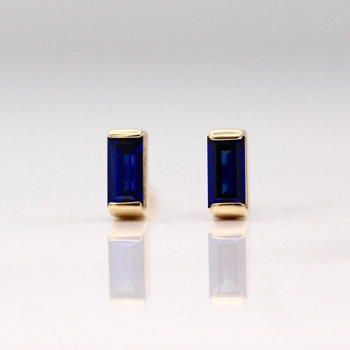 The September Baguette Birthstone Earrings with Blue Sapphire in Yellow Gold against a white background