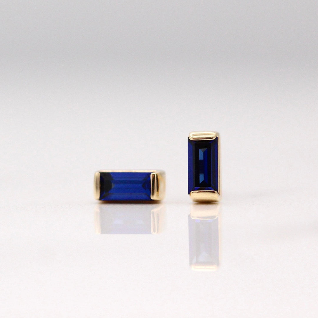 The September Baguette Birthstone Earrings with Blue Sapphire in Yellow Gold against a white background