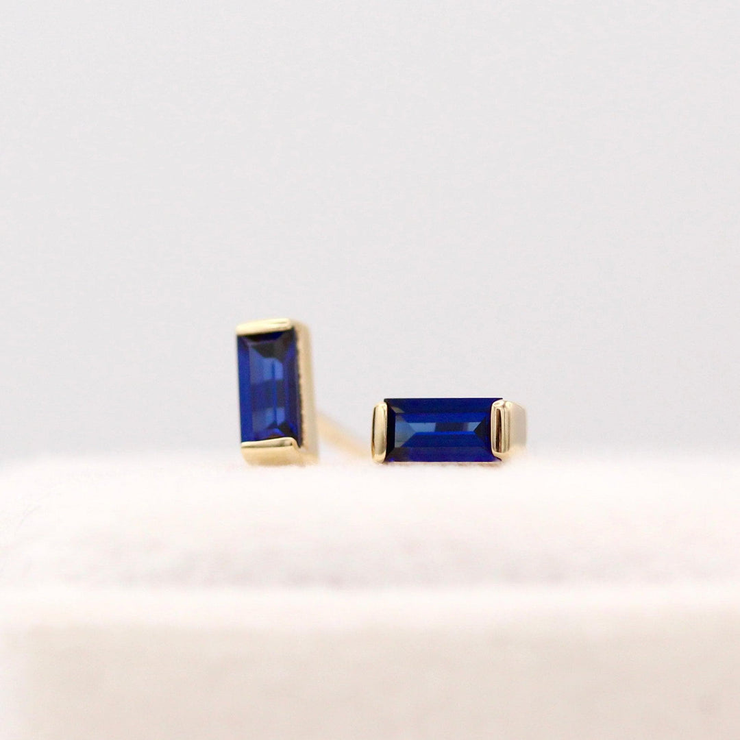The September Baguette Birthstone Earrings with Blue Sapphire in Yellow Gold atop of a white velvet ring box