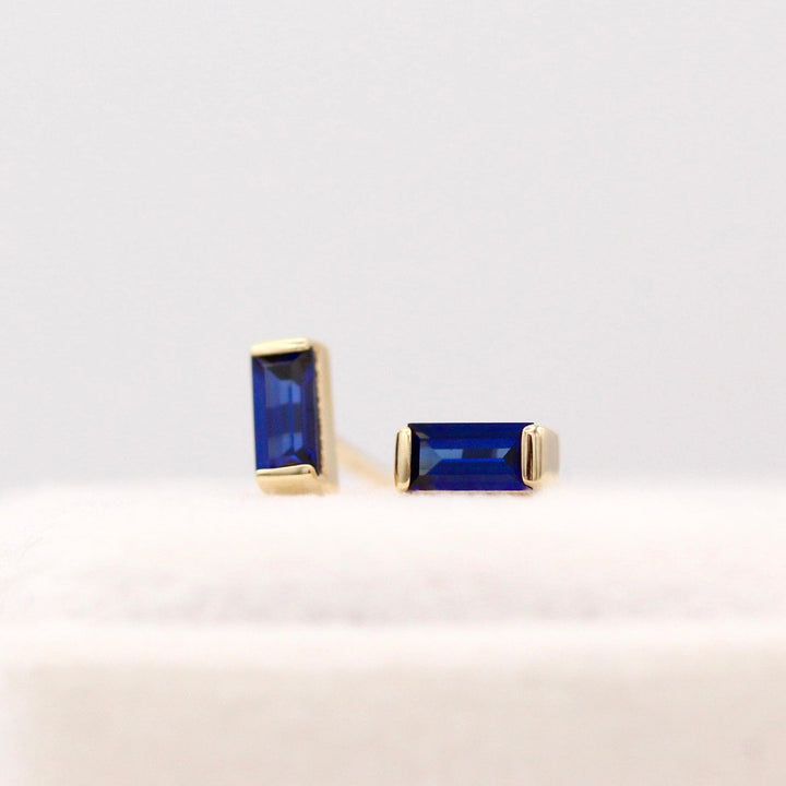 The September Baguette Birthstone Earrings with Blue Sapphire in Yellow Gold atop of a white velvet ring box