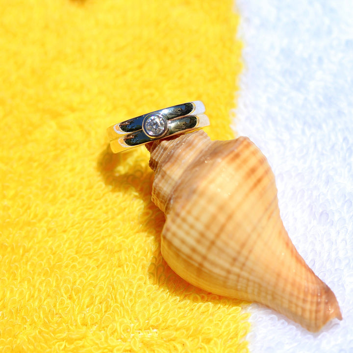 Two tone gold ring with a diamond on a seashell against a yellow and white background