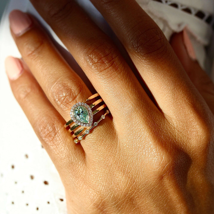 The Chelsea Ring in Yellow Gold with Aqua Moissanite stacked with the Sloane wedding band in yellow gold modeled on a hand