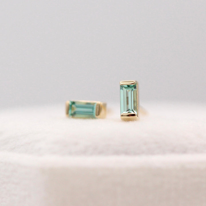 The August Baguette Birthstone Earrings with Chrysoberyl in Yellow Gold atop of a white velvet ring box