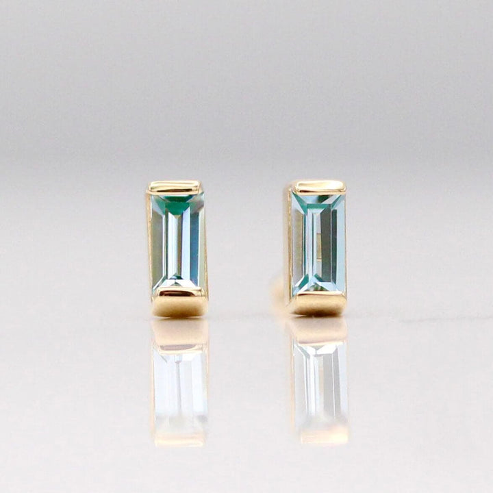 The March Baguette Birthstone Earrings with Aqua Spinel in Yellow Gold against a white background