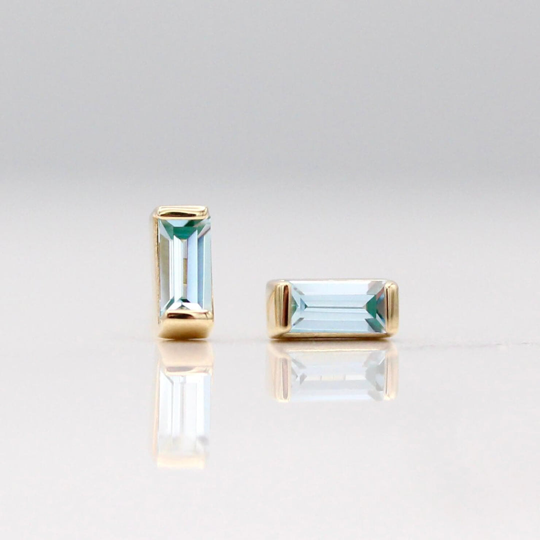 The March Baguette Birthstone Earrings with Aqua Spinel in Yellow Gold against a white background