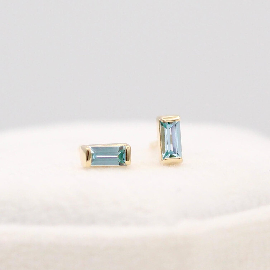The March Baguette Birthstone Earrings with Aqua Spinel in Yellow Gold atop of a white velvet ring box