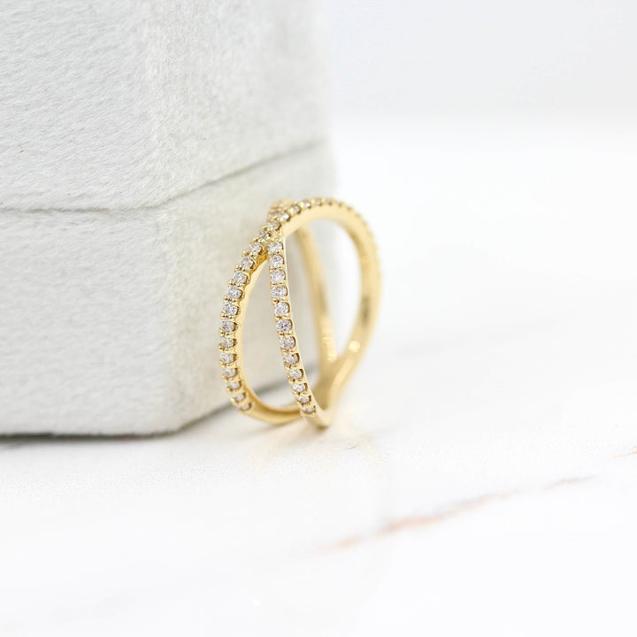 The Criss Cross ring in yellow gold leaning against a white velvet ring box