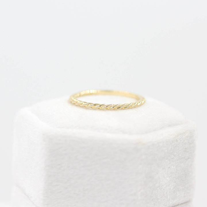 The Dainty Twist Stacking Ring in Yellow Gold atop a white velvet ring box