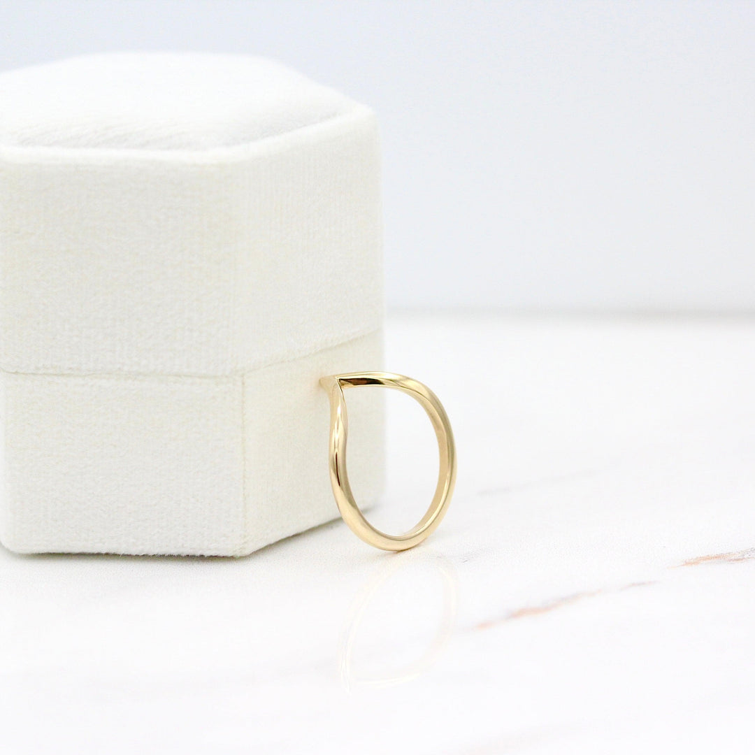 The Deep V Wedding Band in Yellow Gold leaning against a white velvet ring box