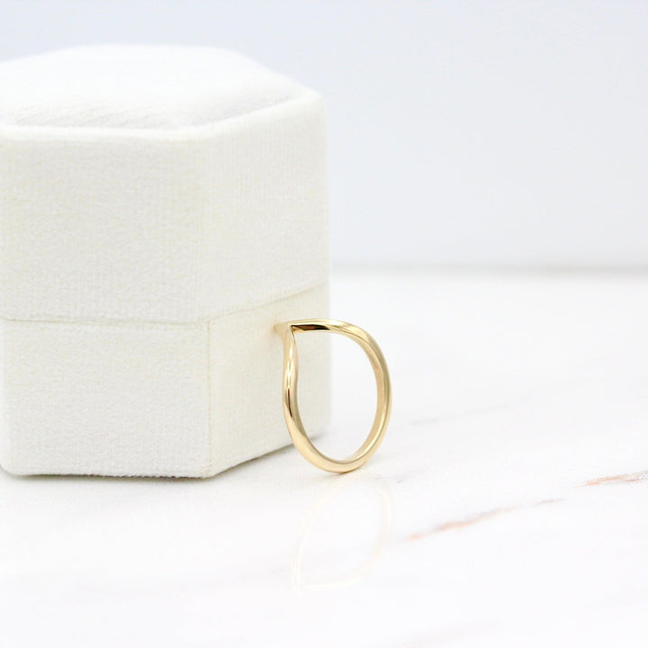 The Deep V Wedding Band in Yellow Gold leaning against a white velvet ring box