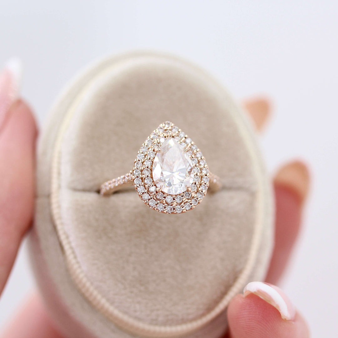 The Double-Halo Carly Ring in Rose Gold in a white velvet ring box held by a hand