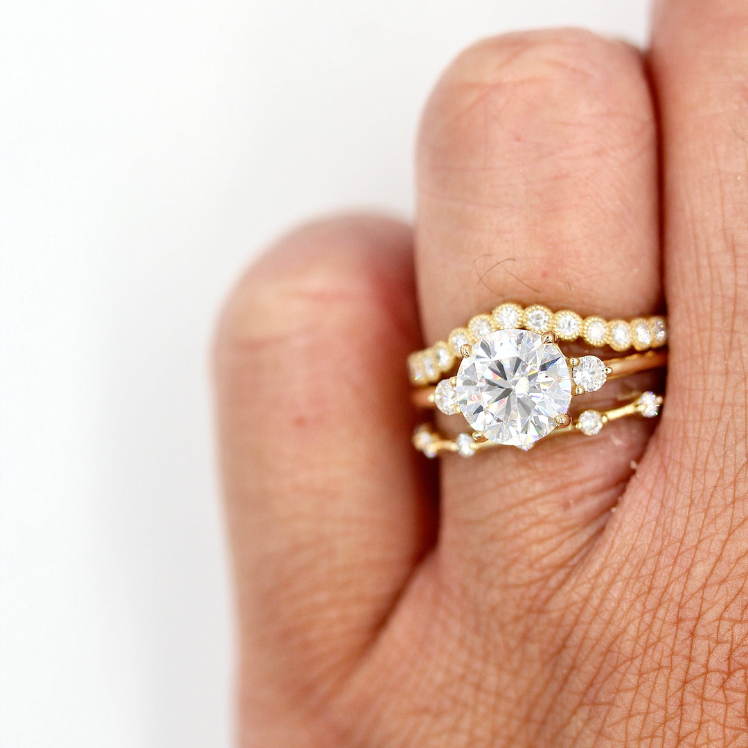 The Esme Ring (Round) in Yellow Gold stacked with the Florence Contour Band in yellow gold and the Sloane Wedding Band in yellow gold against a white background