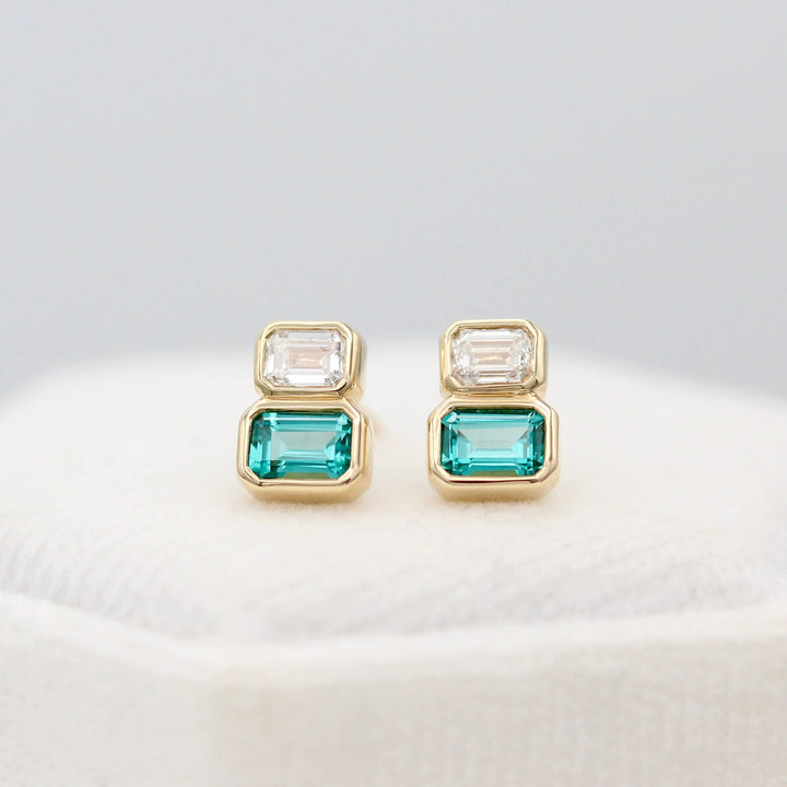 The Emerald-Cut Diamond and Paraiba Spinel Two-Stone Earrings in Yellow Gold atop of a white velvet ring box