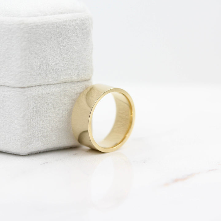 Flat Men's Band/Unisex Band in Yellow Gold leaning against a ring box