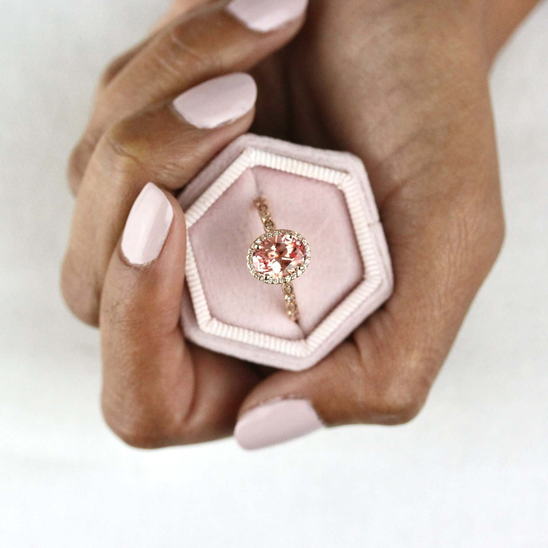 Hand holding pink velvet ring box with rose gold peachy-pink sapphire ring