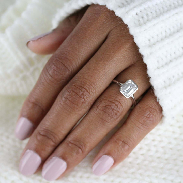 Hand wearing emerald-cut moissanite in a delicate white gold bezel ring