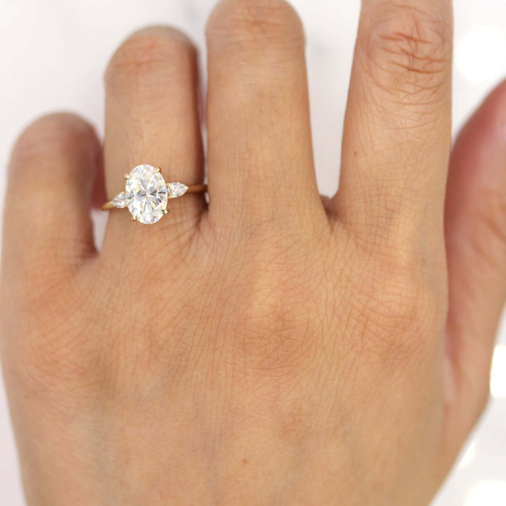 Hand wearing oval three-stone engagement ring with pear accents