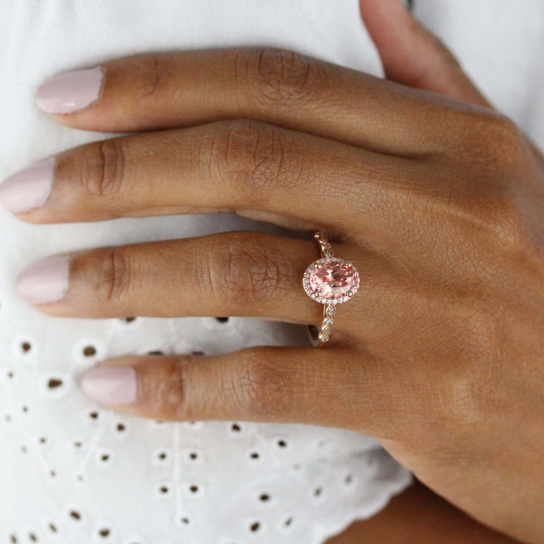 Hand wearing peachy-pink sapphire ring in vintage setting