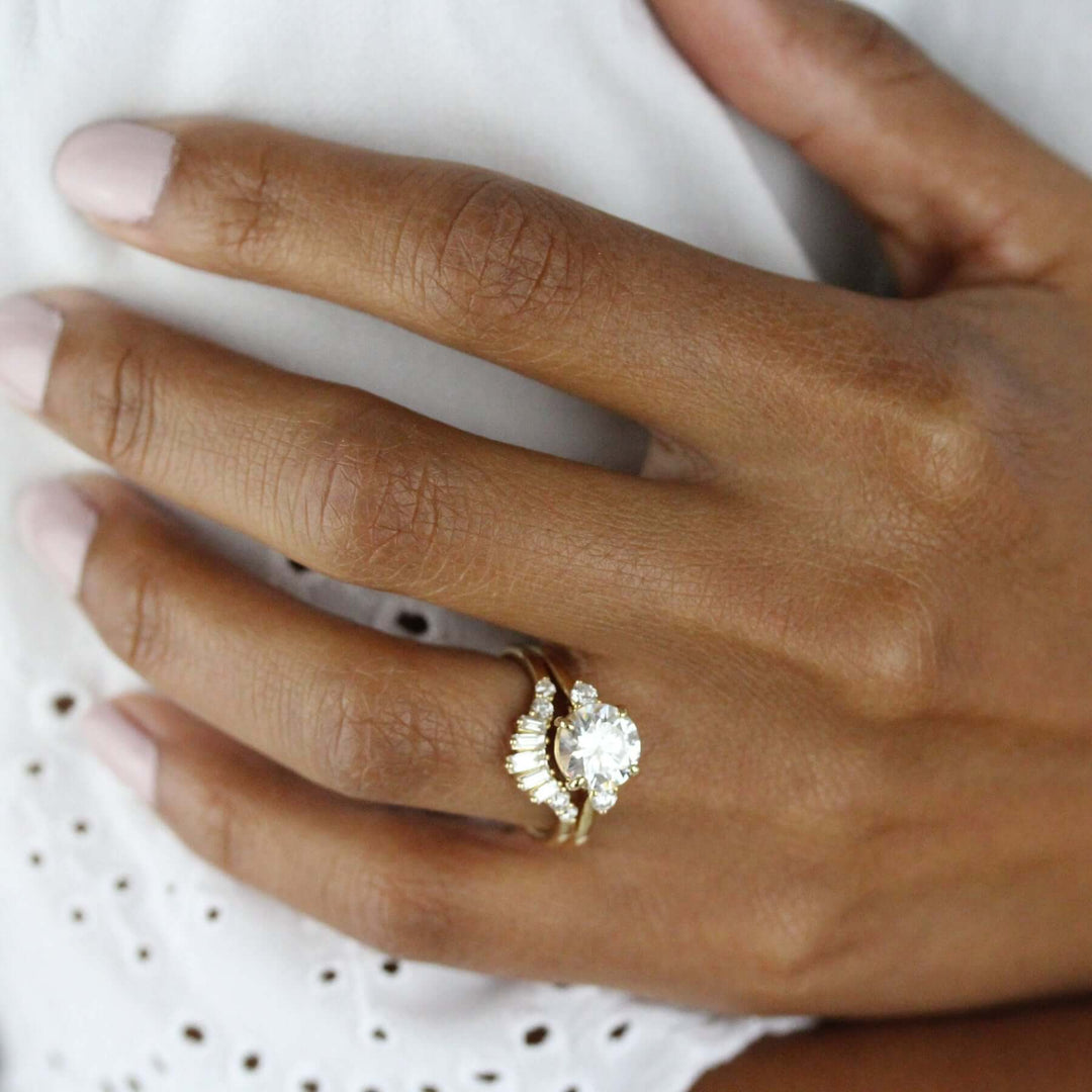 Hand wearing sparkling three-stone engagement ring paired with baguette lab-grown diamond wedding band 