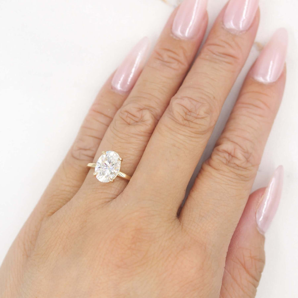 Hand with pink nails wearing oval solitaire engagement ring