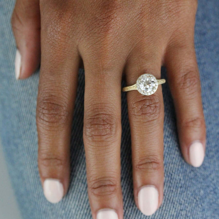Hand wearing yellow gold antique-style halo engagement ring