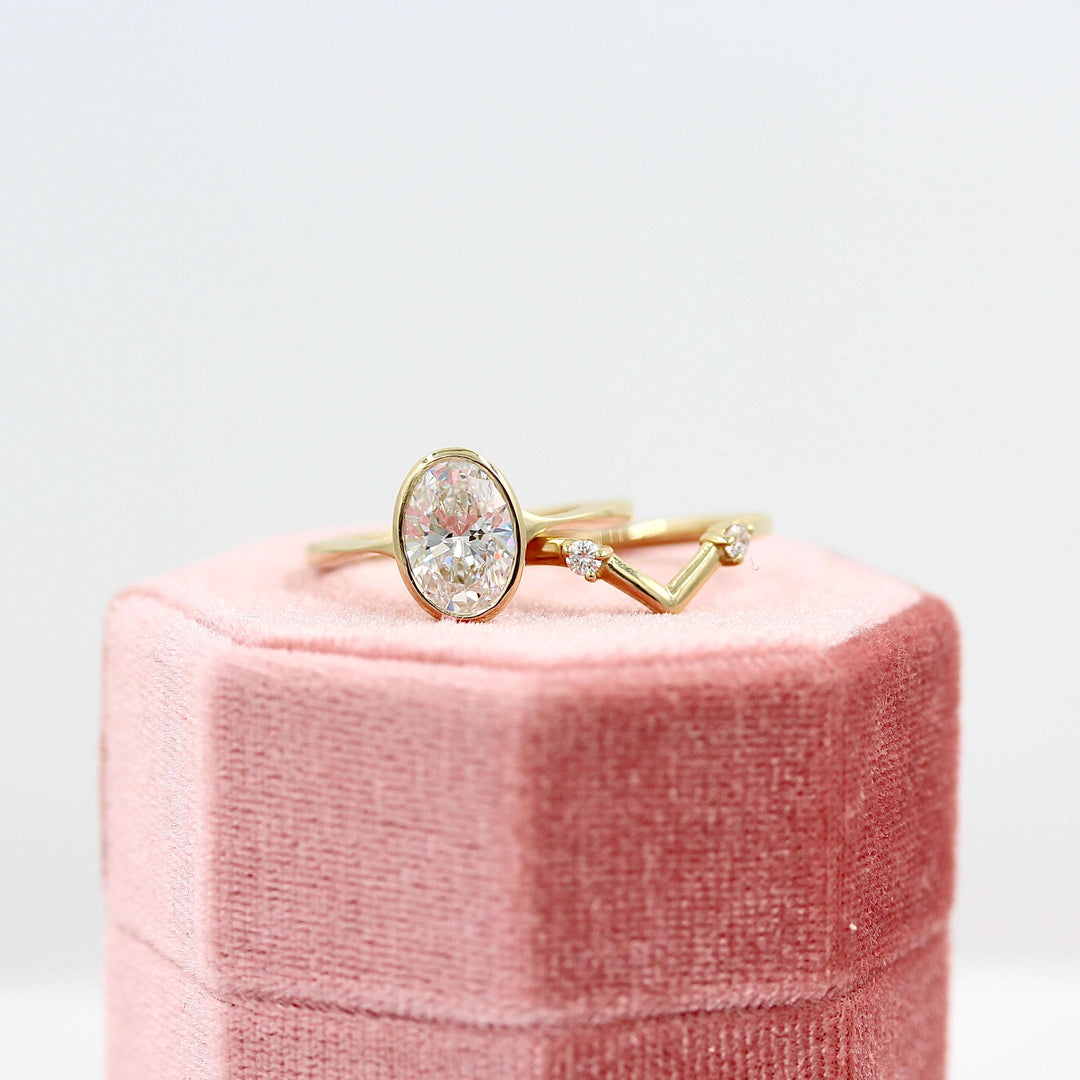 The Stevie Ring (Oval) in Yellow Gold with Lab Grown Diamond stacked with the Double Diamond V-Band in yellow gold atop a pink velvet ring box