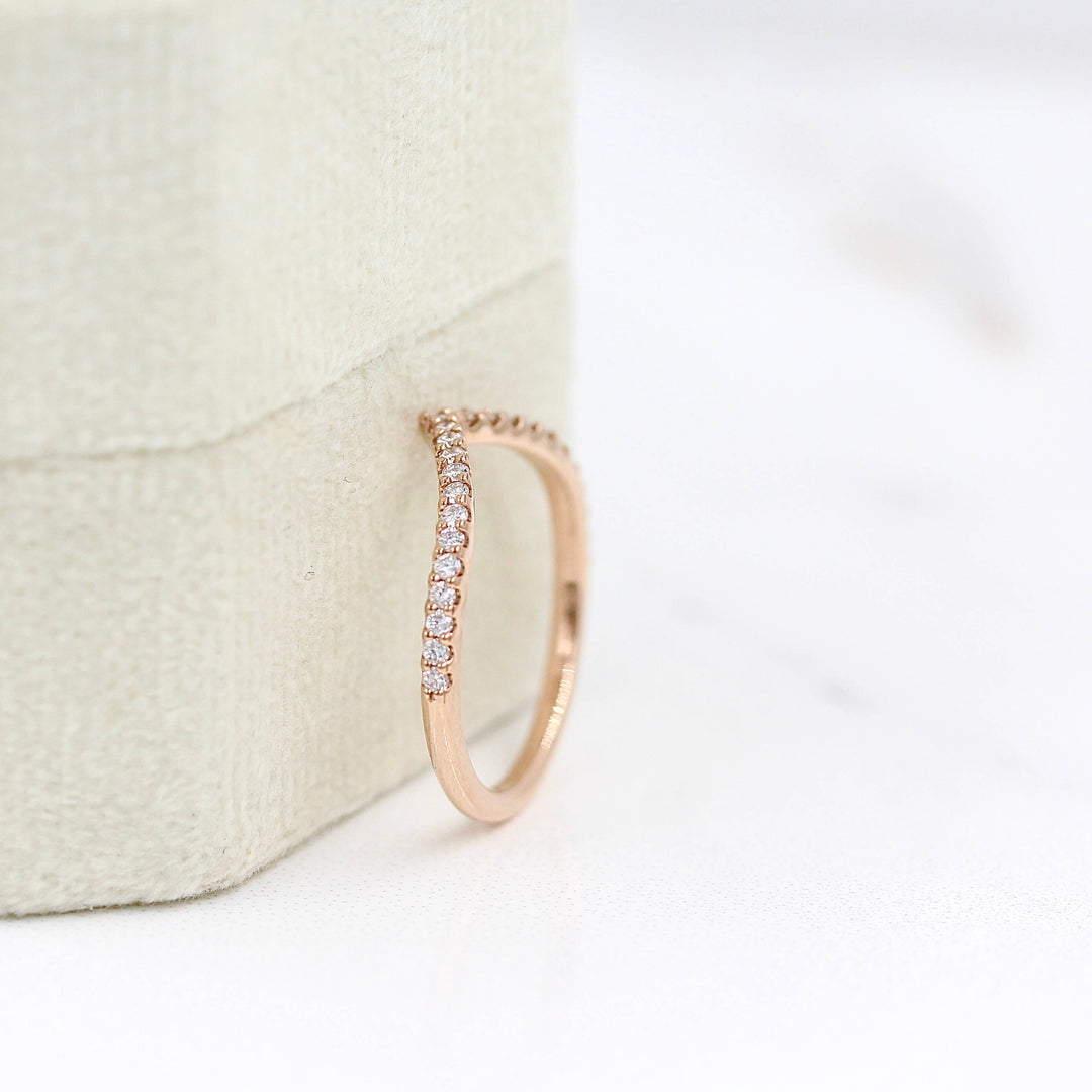 The Diamond V-Band in Rose Gold leaning against a tan velvet ring box