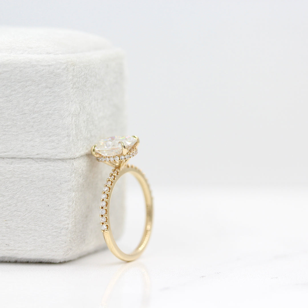 The Paris Hidden Halo Ring (Cushion) in yellow gold leaning against a white velvet ring box