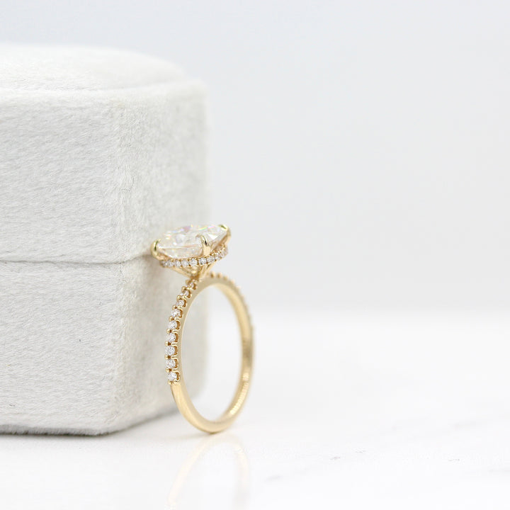 The Paris Hidden Halo Ring in Yellow Gold with 2ct Moissanite leaning against a white velvet ring box