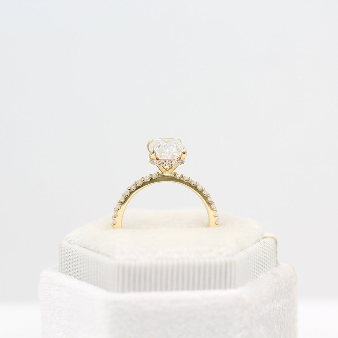 The Paris Hidden Halo Ring (Cushion) in yellow gold leaning in a white velvet ring box