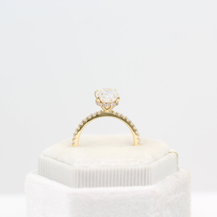 The Paris Hidden Halo Ring (Cushion) in yellow gold leaning in a white velvet ring box